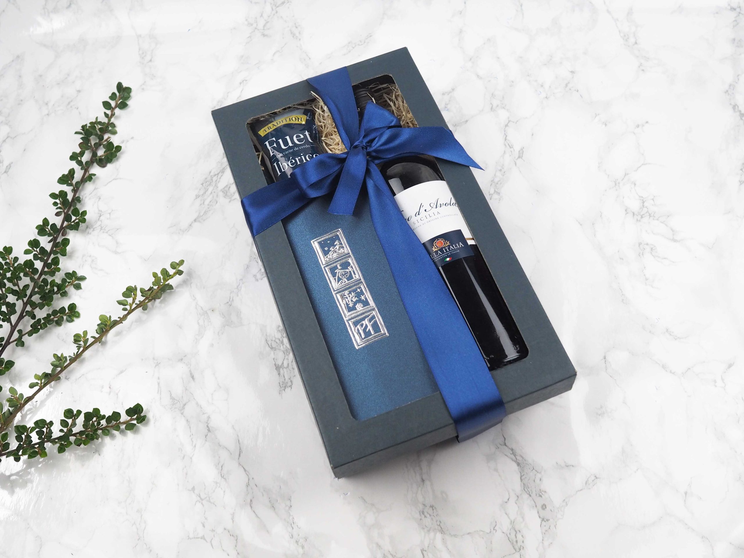 Dárkový balíček Blue Avola v sobě obsahuje novoročenku, fuet Ibérico a červené italské víno Nero di Avola.